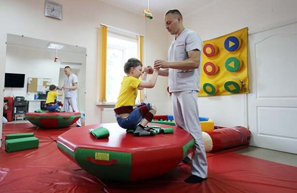 Physical Therapist helping a child with disabilities through therapy on a medicine ball.